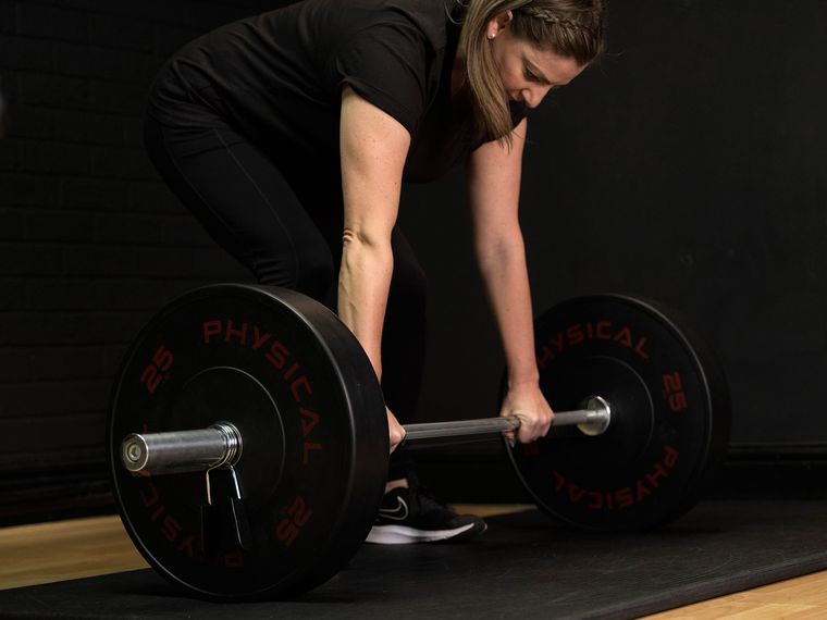 Elin Wyn guiding a client’s grip on a loaded barbell before a deadlift